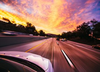 Descubre siete formas que tienen los ‘malos’ de ciberatacar tu coche Vista del capó de un coche que circula por una autopista hacia el amanecer