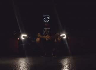 Cuatro sustos que te pudo dar el coche en Halloween Imagen nocturna de una persona con una careta de Halloween, situada en cunclillas delante de un coche con las luces encendidas