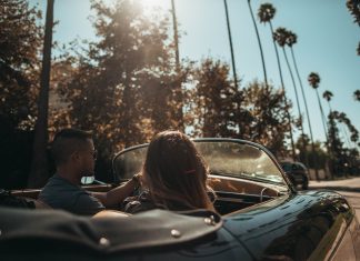 ¿Cuánto hay que esperar para que llegue el coche autónomo? Dos jóvenes montados en un descapotable conducen por una avenida de palmeras en un día soleado