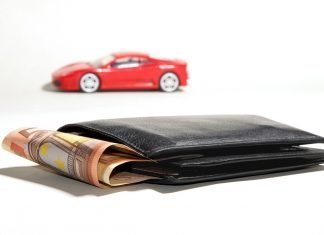 ¿Vendes o buscas coche por Wallapop? Deberías prestar atención a esto Primer plano de una cartera de la que asoma un fajo de billetes de 50€, con la miniatura de un Ferrari rojo al fondo
