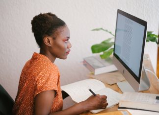 Por qué debes seguir estos blogs de ciberseguridad Una mujer lee el ordenador sentada en una mesa mientras toma notas en una libreta