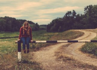 Restringir el tráfico en ciudad: ¿es una buena idea? Una chica está sentada sobre una barrera que bloquea el paso en un camino de tierra en mitad del campo