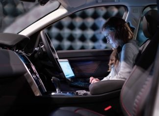 La pregunta básica: ¿qué es un coche conectado? Una mujer está sentada en el asiento del copiloto de un coche conectado con un ordenador sobre las piernas