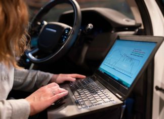 Qué es SOA, y por qué lo necesitan los coches conectados Centro ciberseguridad coches: una mujer consulta un ordeandor portátil sentada en el asiento del copiloto de un coche