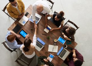 De bombillas a coches: los objetos cotidianos que te pueden crackear Seguridad dispositivos conectados: imagen cenital de un grupo de personas sentadas en torno a una mesa, todas ellas usando un ordenador o un teléfono móvil