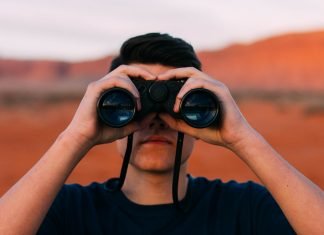 ¿Quién se preocupa de evitar que las flotas de coches sean atacadas? Imagen de un hombre joven, en mitad de un desierto, mirando al horizonte a través de unos prismáticos negros.