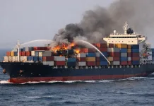 Las baterías son el futuro de los eléctricos, pero… ¿por qué nadie quiere transportarlas? Imagen de un carguero en alta mar con contenedores y un fuego
